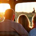 A happy family smiling during a safari, with a giraffe in the background.